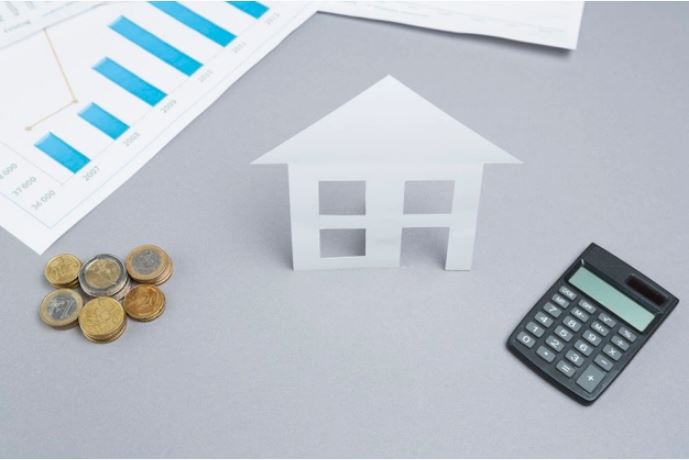 Petite maquette de maison en papier avec pièces de monnaie et calculatrice, près des graphiques, illustrant l’organisation de son déménagement.